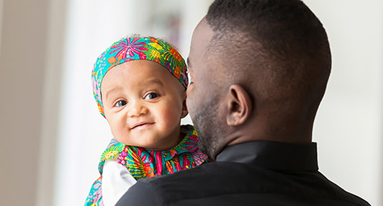 A person holding a small child who is smiling and looking into the camera