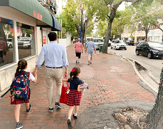 A person walking hand-in-hand with two children down a street